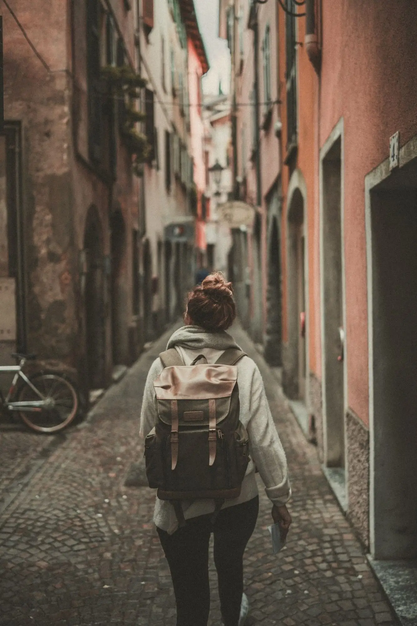 A traveller with a backpack walking down a narrow, sunlit old-town street