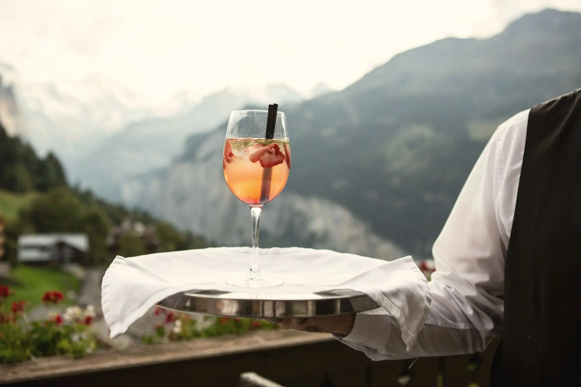 A waiter carrying a chilled drink on a silver tray on a terrace high in the mountains