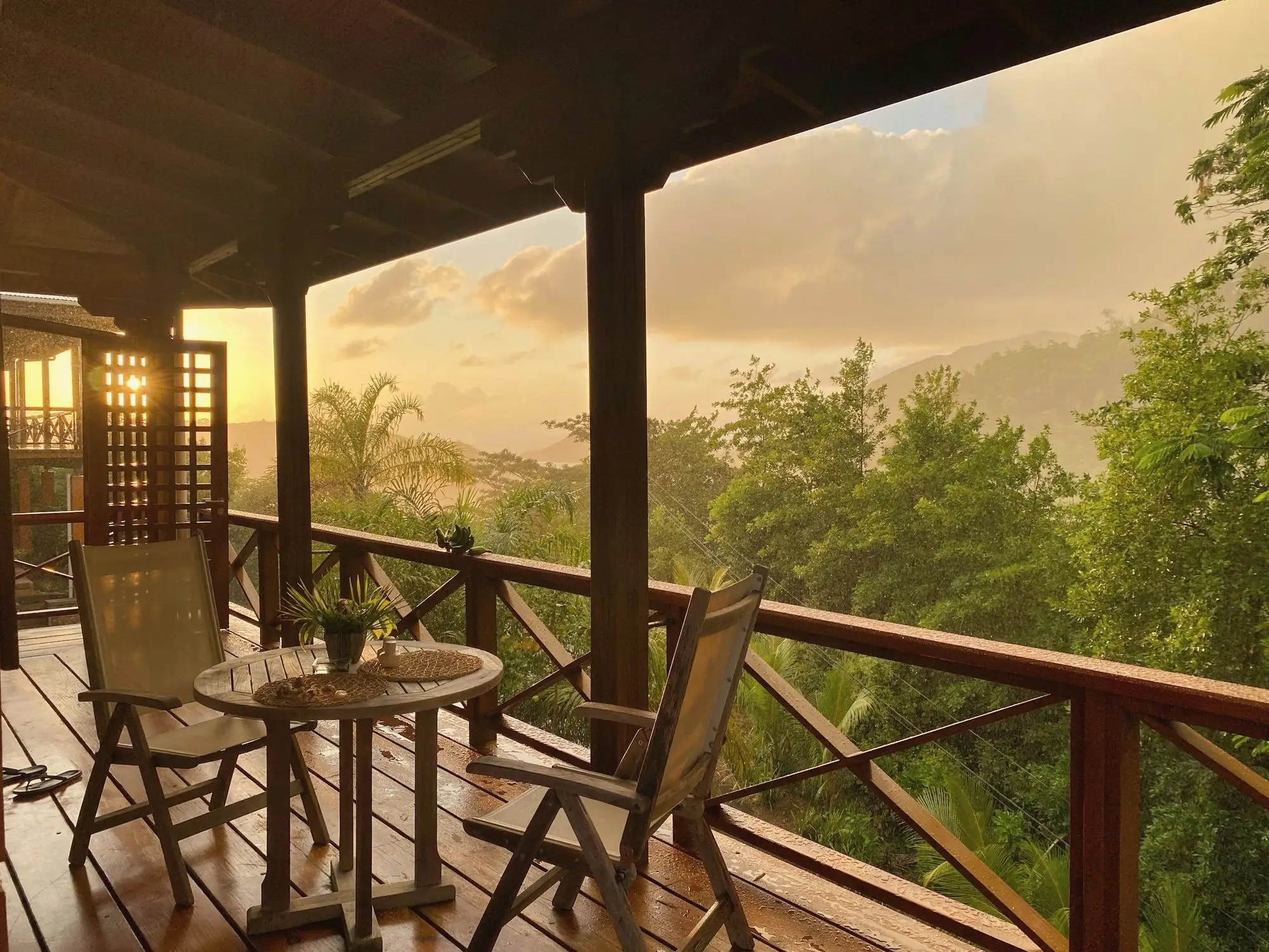 A timber veranda with two chairs overlooking a forested valley in warm evening light