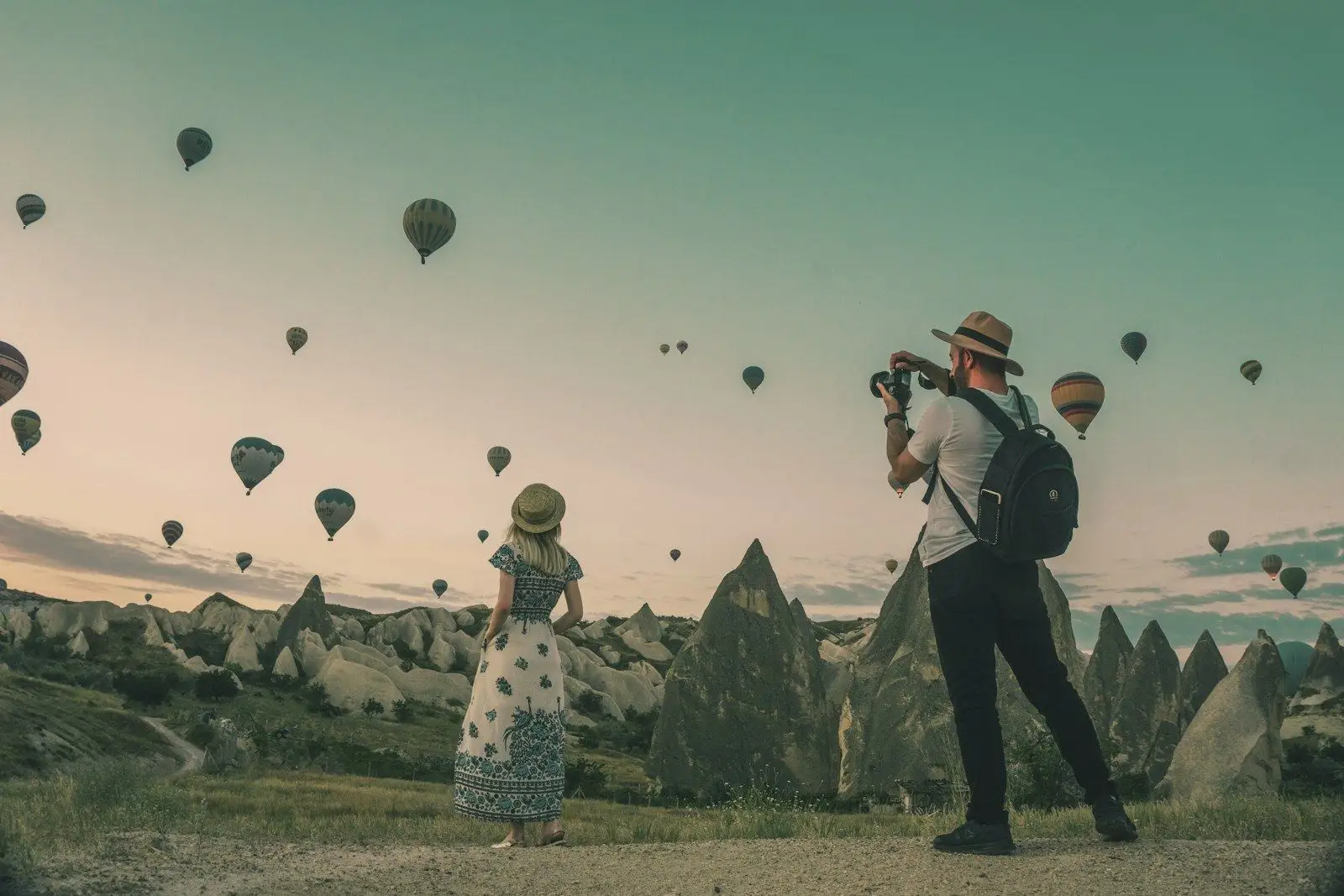 A couple watching hot-air balloons rise over a valley at dawn