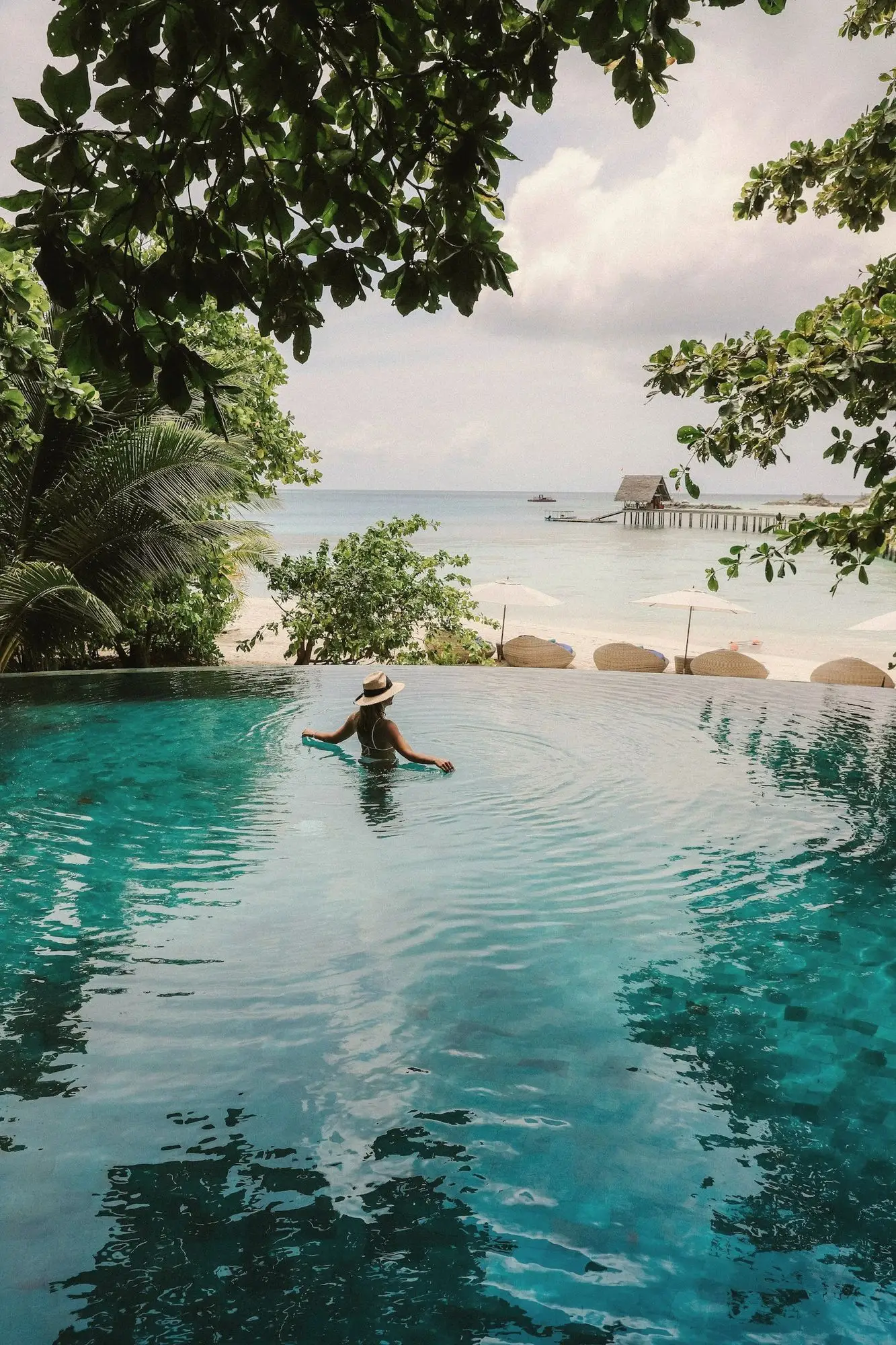 A guest relaxing in an infinity pool that melts into a pale tropical sea