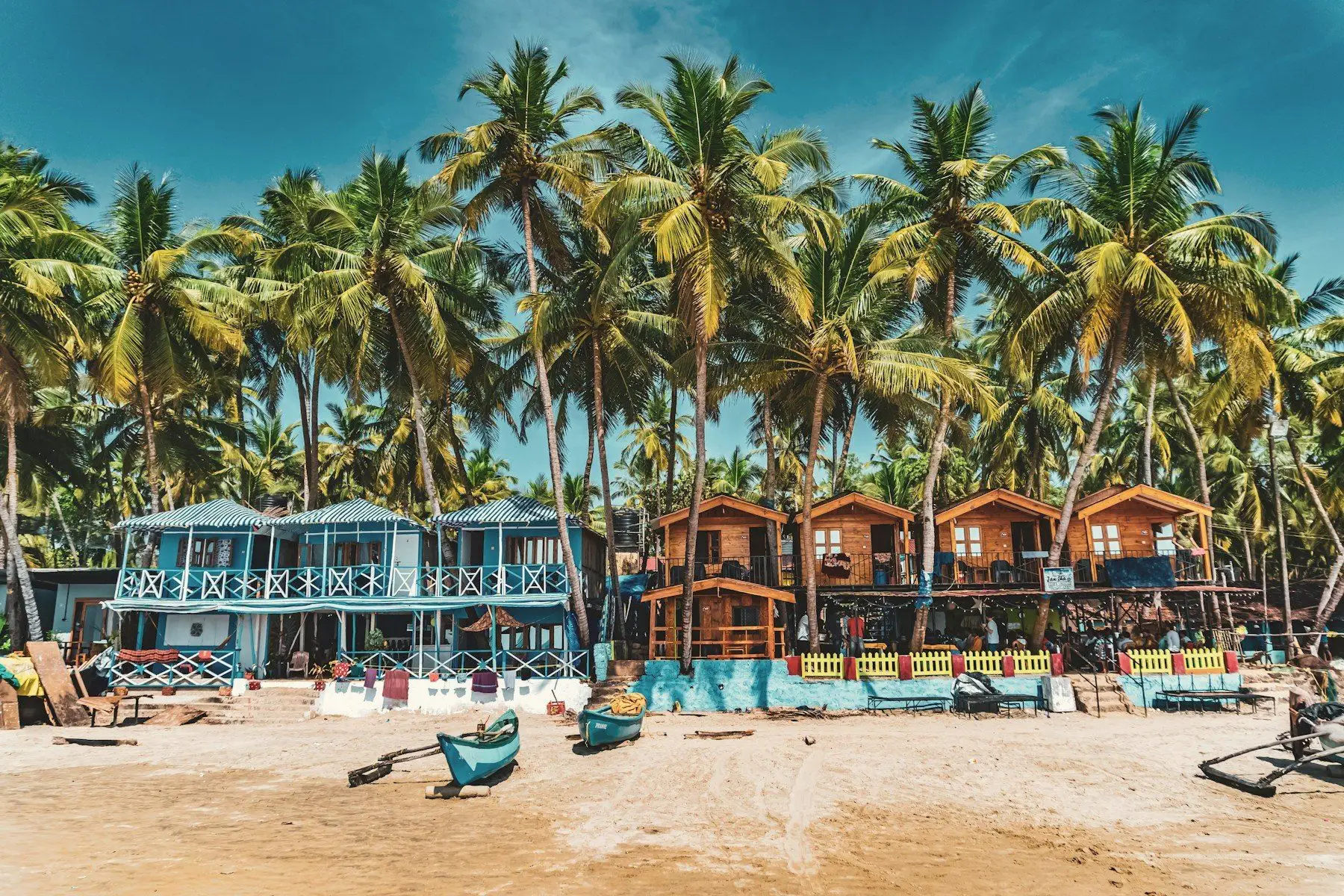 Colourful beach huts beneath tall palms on a Goan beach