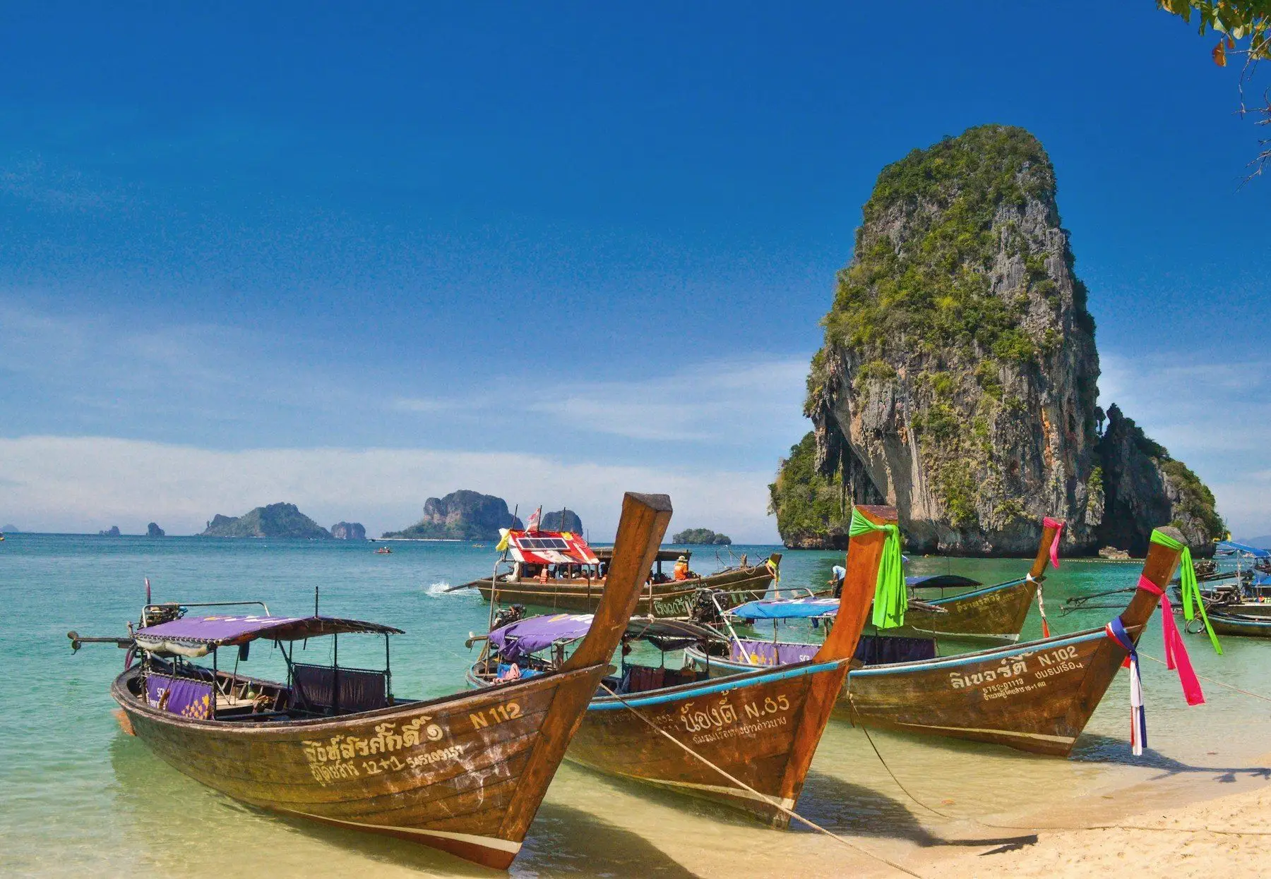 Long-tail boats beside limestone cliffs on a Krabi beach