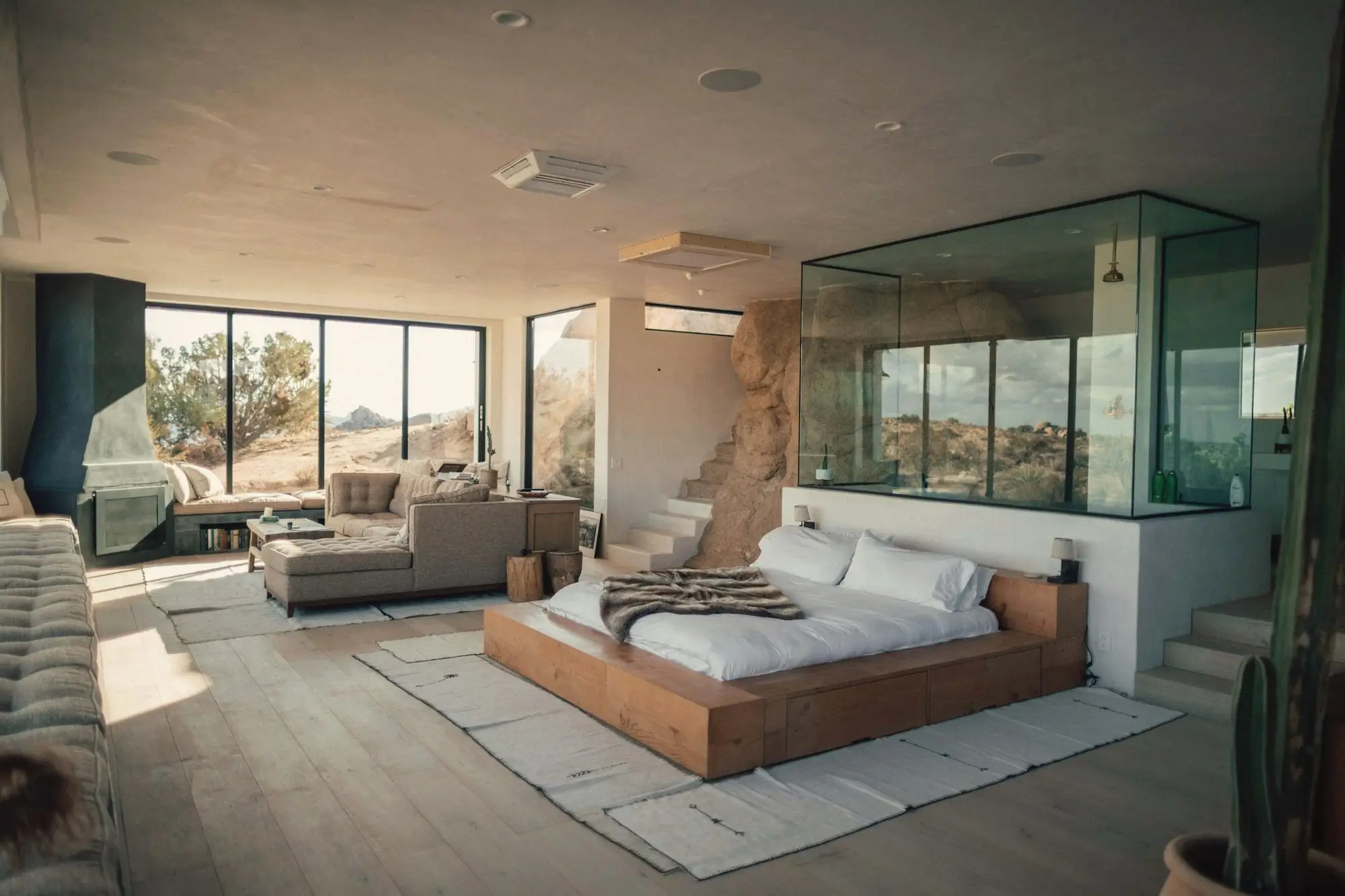 A light-filled modern suite with a timber platform bed, glass-walled bathroom and desert views