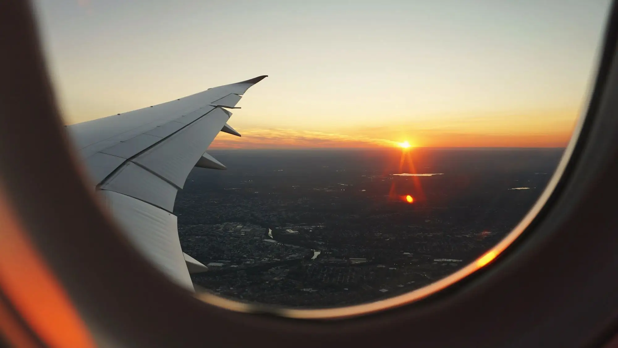 Sunset over a patchwork of land seen through an aircraft window, the wing catching the light