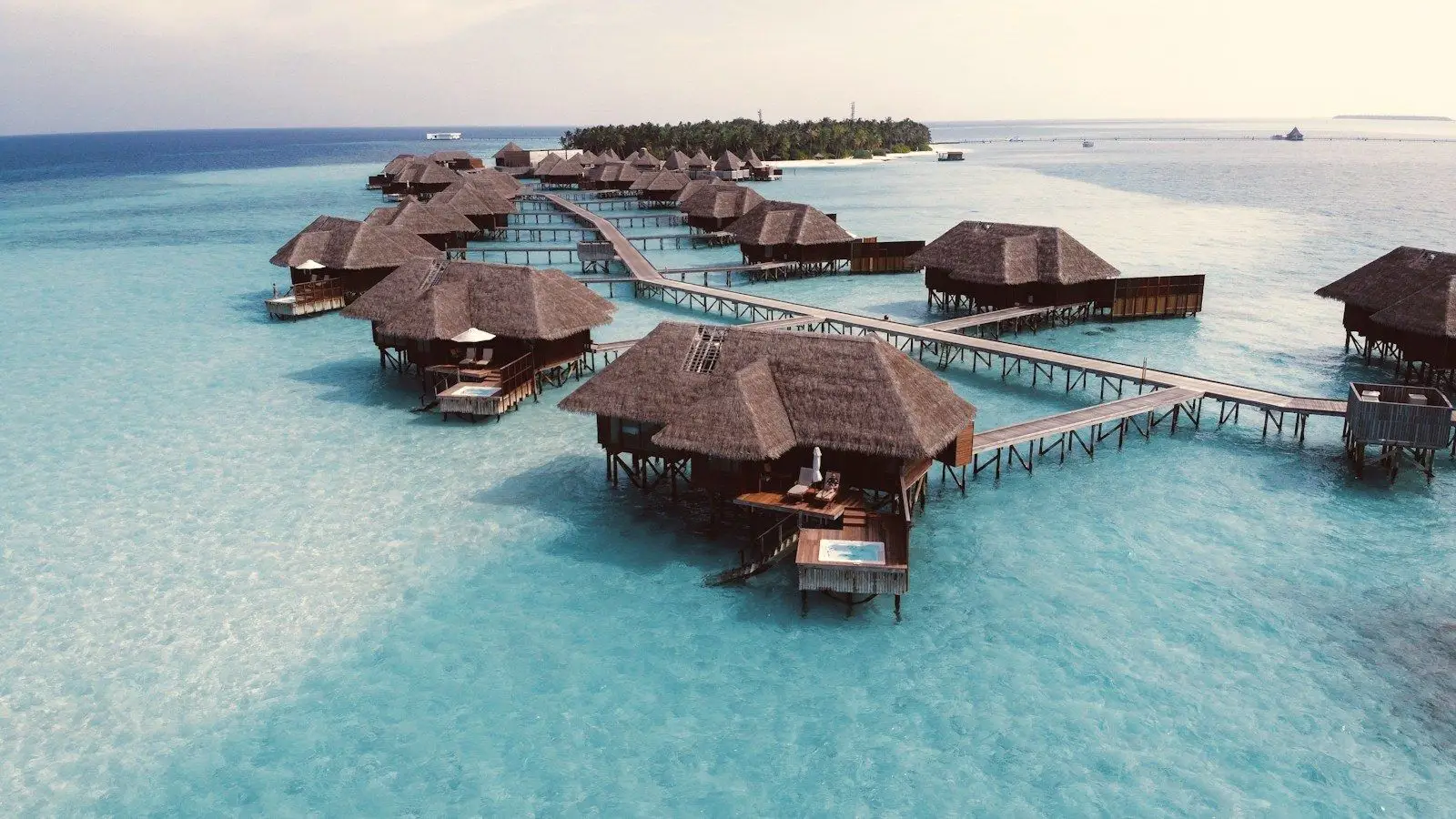 Thatched overwater villas connected by a wooden walkway over a clear lagoon