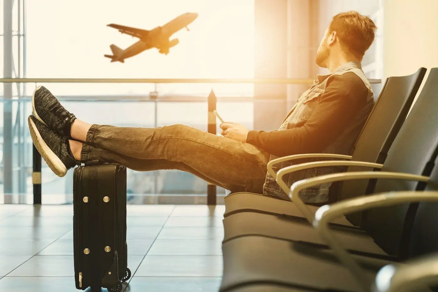 A relaxed traveller with feet up on a suitcase in an airport lounge as a plane takes off outside
